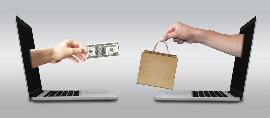 Two hands reaching to each other from two computers. The one is holding money and the other is holding a bag with some products
